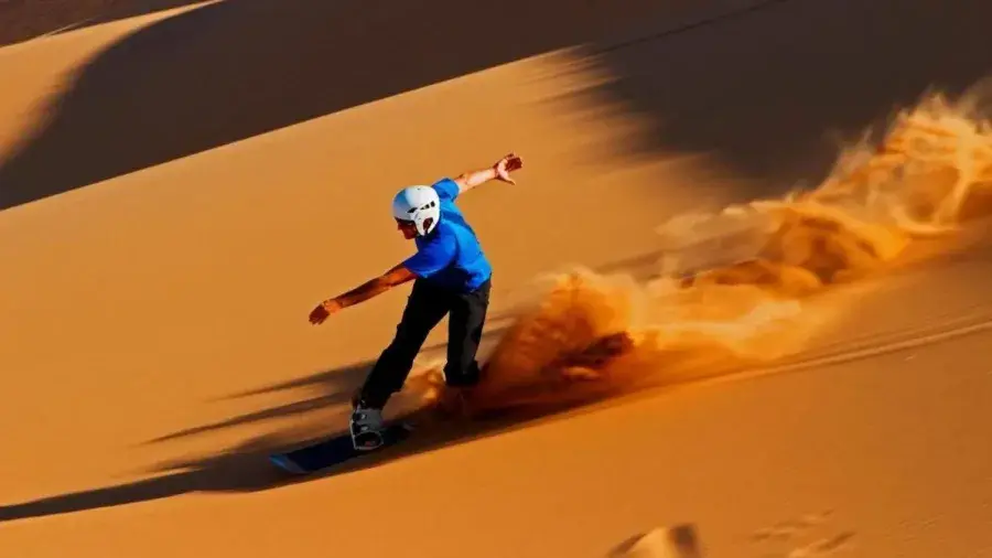 Traveler sandboarding on a tall Erg Chigaga dune